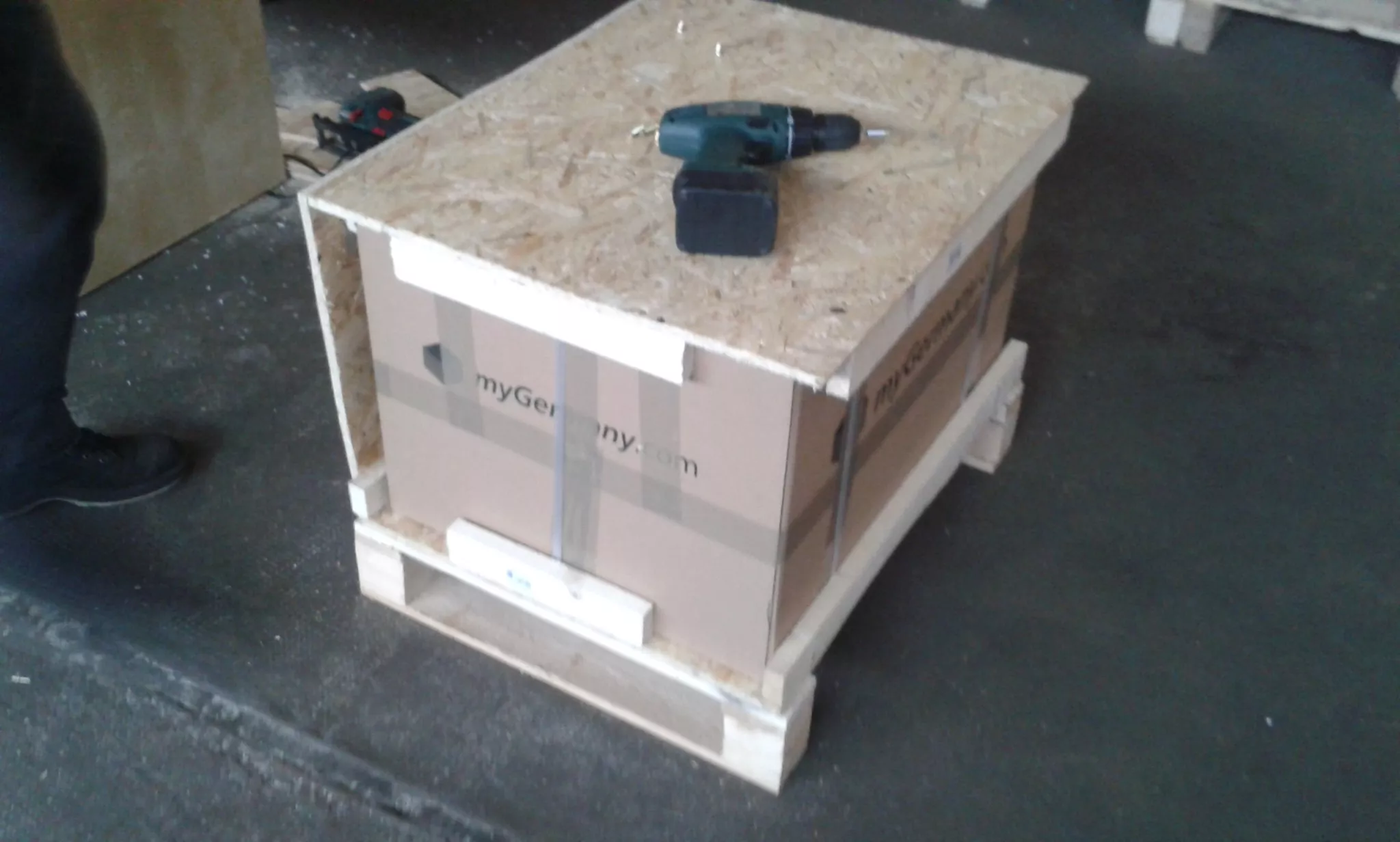 wooden crate containing packaged box with power drill placed on top